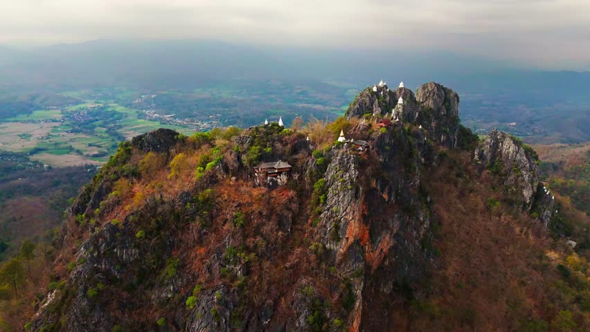 Mountain ridges crowned with hilltop shrines at Wat Chaloem Phra Kiat in Thailand at sunrise, aerial