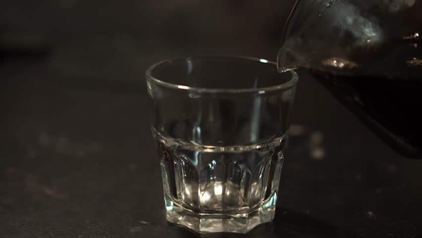 Pouring Freshly Brewed V60 Coffee from Server into Glass Cup. Close-up of hand pouring freshly brewed V60 coffee from a glass server into a transparent cup, highlighting rich color and clarity.