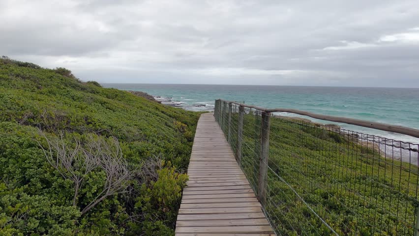 POV walking boardwalk footpath through dunes to sand beach, grey cloud