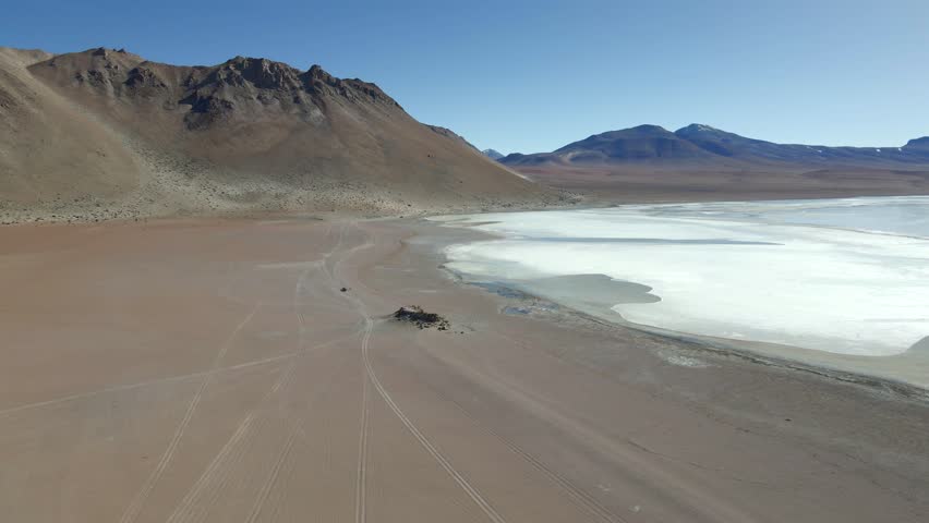 Drone over pale Laguna Chiar Kkota with mirrored volcanic backdrop and red terrain