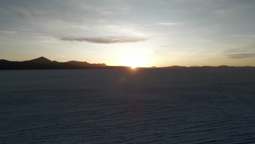 High aerial panoramic dolly of wide salt flat at Uyuni with mirrored sky and light horizon, silhouette mountains