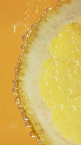 Vertical video of lemon slice in fizzy soda with bubbles rising along peel, highlighting freshness, citrus energy and vibrant motion.