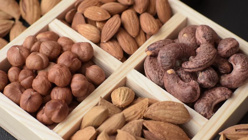 Wooden box with four sections filled with nuts almonds, shelled almonds, cashews, hazelnuts