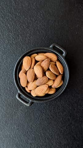Roasted or raw peeled almonds in bowl on dark concrete background
