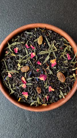 Dry tea mix blend black, green and flower petals in bowl on dark concrete background