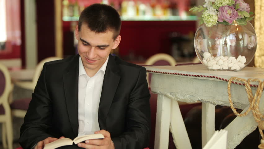 Man reading a book and smiling in cafe