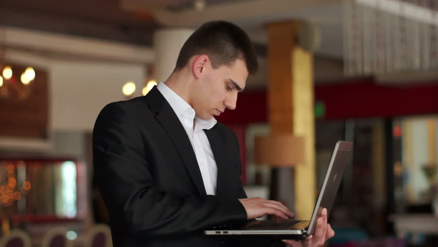 Young adult typing on a laptop and looking away smiling