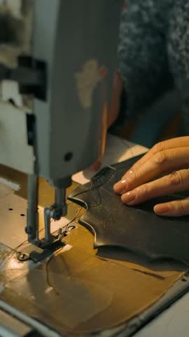 Unrecognizable woman handles woven seam by hand on new leather bag behind loom. The work of the master in the assembly of leather products on a sewing machine. Vertical shot.