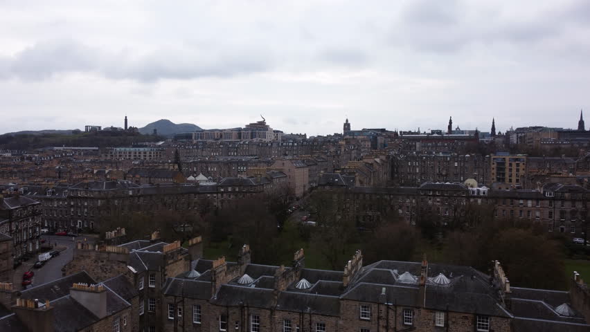 Aerial tracking shot of a park and the cityscape of Old Town Edinburgh, gloomy day