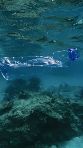 A discarded plastic bottle floating in sea. Underwater pollution endangers marine life and disrupts the balance of the aquatic environment. Vertical video