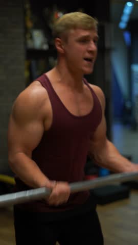 Muscular bodybuilder guy doing exercises in gym. Concept of willpower, motivation and passion. 4k Vertical shot 