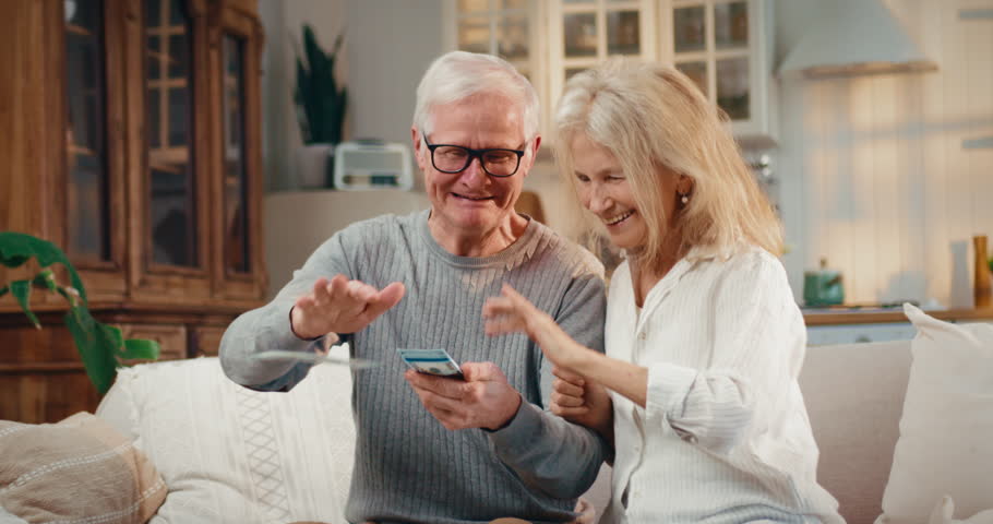 Happy old spouses throwing money around, portrait of rich people at home. Pension benefits for retirees, richness and wealth, aged woman and man playing with cash dollars, happy aging and retirement