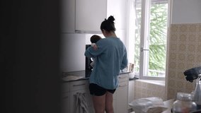 Back of Mother holding baby while preparing food in a bright kitchen, exemplifying multi-tasking and balancing parenting with daily chores, love and care in a modern home setting - Powered by Shutterstock - Get 15% off with code: PIKWIZARD15