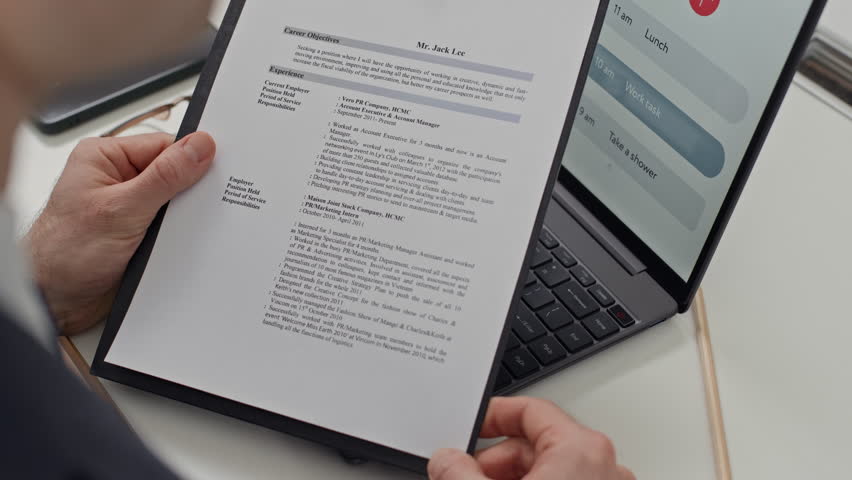 Cropped shot of male employee holding folder with CV of candidate when sitting in front of laptop at table during job interview at office