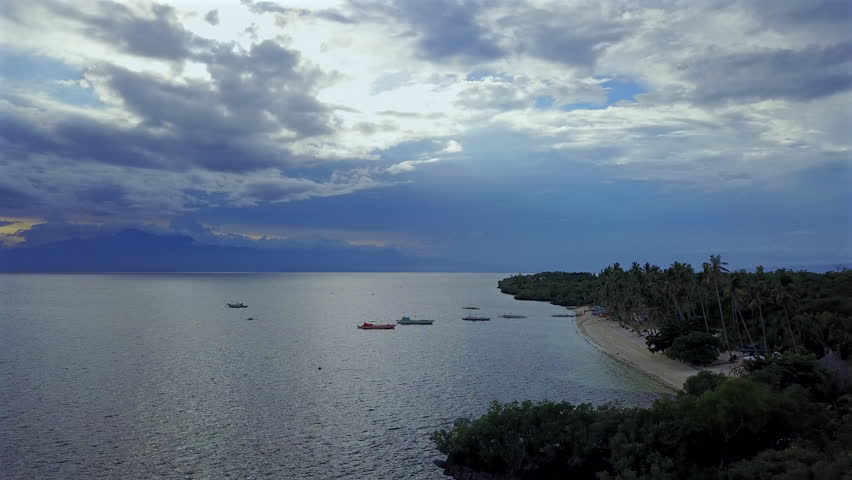 Frontal traveling shot in the coastal area of Siquijor Island, Philippines, close to sunset. Captures the serene seascape, boats, and the changing light of the approaching evening