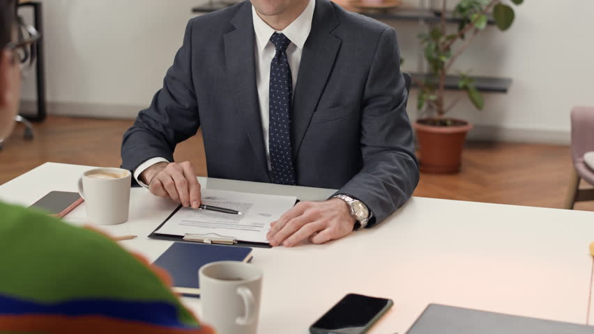 Medium shot of adult HR manager shaking hand of young male applicant drinking tea during job interview
