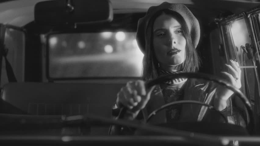 Beautiful woman wearing beret and leather jacket lighting cigarette and smoking while driving vintage car at night, captured in dramatic black and white film noir style
