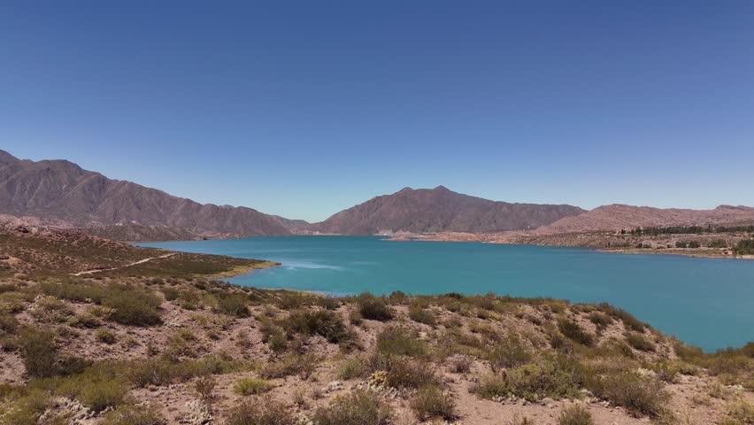 Aerial rising shot of beautiful Lago Potrerillos lake in Mendoza Province in Argentina. Blue sky and mountain range in background.
