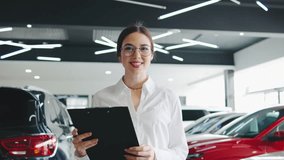 Professional woman smiling while holding a clipboard in a modern car dealership filled with various vehicles during daytime - Powered by Shutterstock - Get 15% off with code: PIKWIZARD15