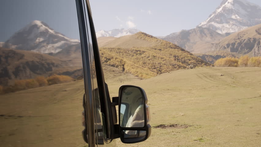 Woman traveler leans out of window of motorhome looking out over captivating mountain landscape