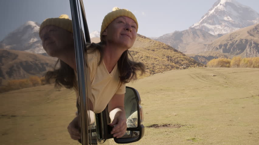 Woman traveler leans out of window of motorhome looking out over captivating mountain landscape