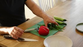 Man preparing fresh vegetables in modern kitchen, organic ingredients. Healthy meal. Cooking Food At Home. Male slicing red pepper and green cucumber on a wooden cutting board. Nutritionist, culinary - Powered by Shutterstock - Get 15% off with code: PIKWIZARD15