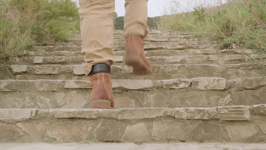 Feet in boots climb up stone steps of stairs outdoors close-up.