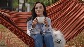A woman enjoys a peaceful and tranquil moment in a cozy hammock with her fluffy little dog, sipping on a warm beverage - Powered by Shutterstock - Get 15% off with code: PIKWIZARD15