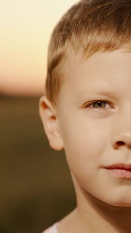 Look kid. Child closeup in front of camera, nature. Portrait of boy looking at camera, standing outdoors in summer park. Smile of child. Face Eyes kind smart kid. Kid boy. Gender of person. Childhood.