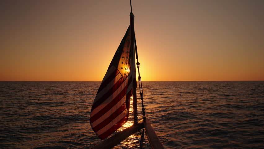Enjoy the breathtaking sunset as the American flag waves on a majestic sailing ship gliding through Key Wests open sea, all captured in stunning slow motion amidst mesmerizing surroundings