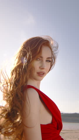 Young Woman With Fiery Locks of Hair, Basking in the Sun. Vertical Camera Captures Her Radiant Smile as She Stands on Beach, Picture of Joy, Contentment. Real person. True Reflection of Beauty.