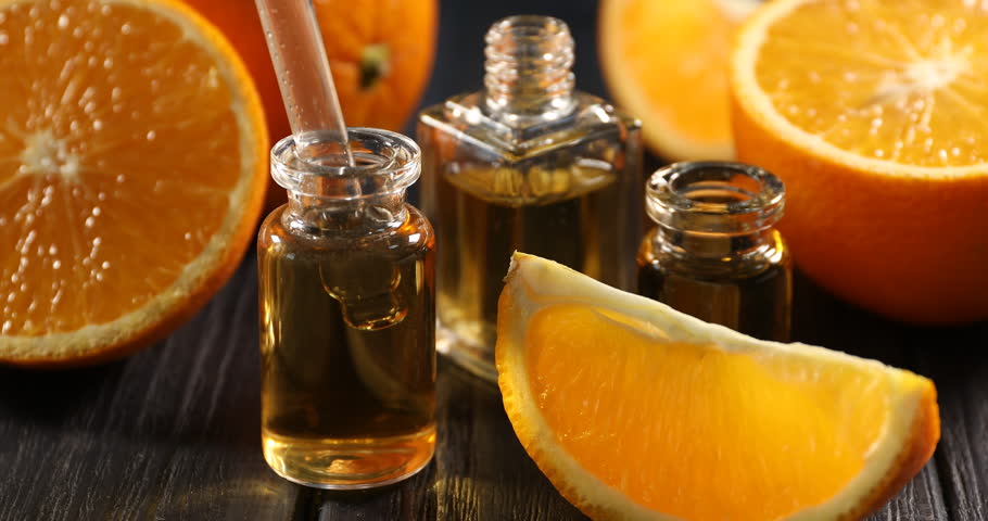 Taking and dripping aromatic essential oil from pipette into perfume bottle among oranges at black wooden table, closeup