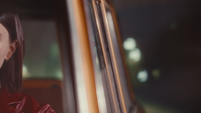 Young feminine woman with red lips driving classic retro car on city street and looking at night road