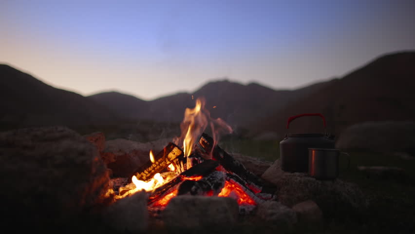 Campfire flame at dusk. Slow motion. Halt for night in mountains in wild deserted area. Beautiful cinematic bonfire flame. Love for nature, hiking in a friendly company, family hiking.