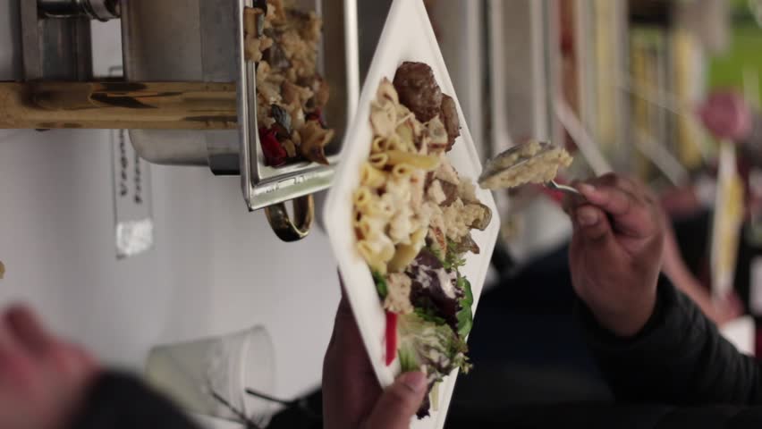 People going down two rows around a long table serving themselves food with a pasta buffet containing alfredo and marinara sauce as well as rice, vegetables and chicken.
