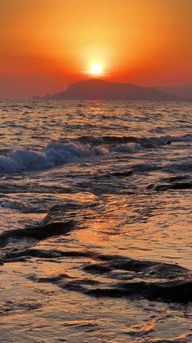 Sunset in Turkey, Alanya. The waves of the Mediterranean Sea roll over the sandy beach. The sunset is reflected in the water and slightly illuminates the city, against the background of Castle Hill.4К
