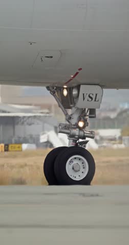 Closeup on the nose wheel of a jetliner as it moves across the runway. Background includes modern airport structures and daylight ambiance.. documenting commercial air travel and transit atmosphere