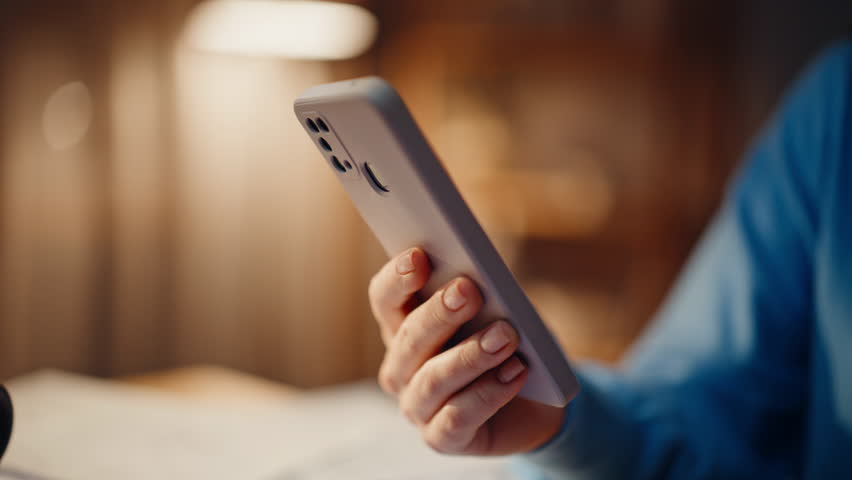 Woman hands tapping smartphone in dark apartment in lamp light closeup. Unrecognizable lady making online purchase by cellphone app in night home. Young freelancer browsing message on mobile phone.