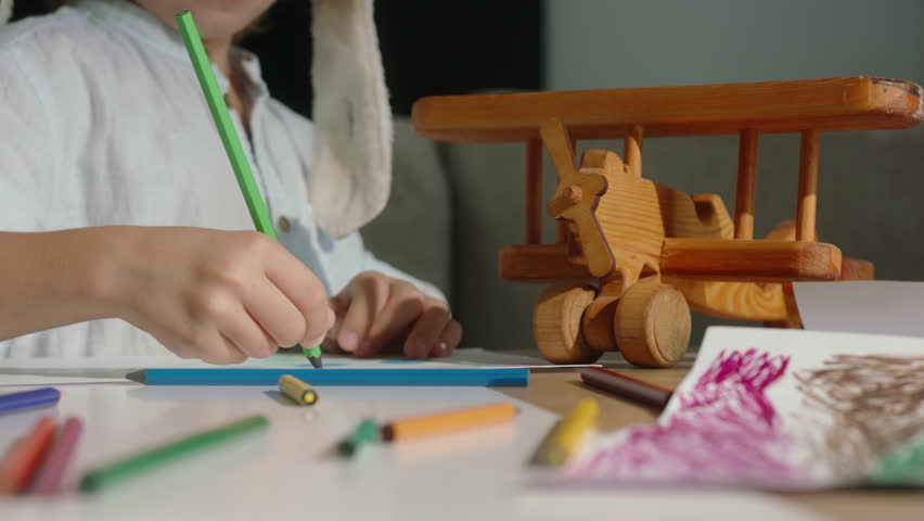 Happy boy in pilot's hat is drawing, wooden plane. Act of drawing, child unearths creative treasures bringing them into physical world. Happy childhood flourishes, artistic brilliance. Kid development