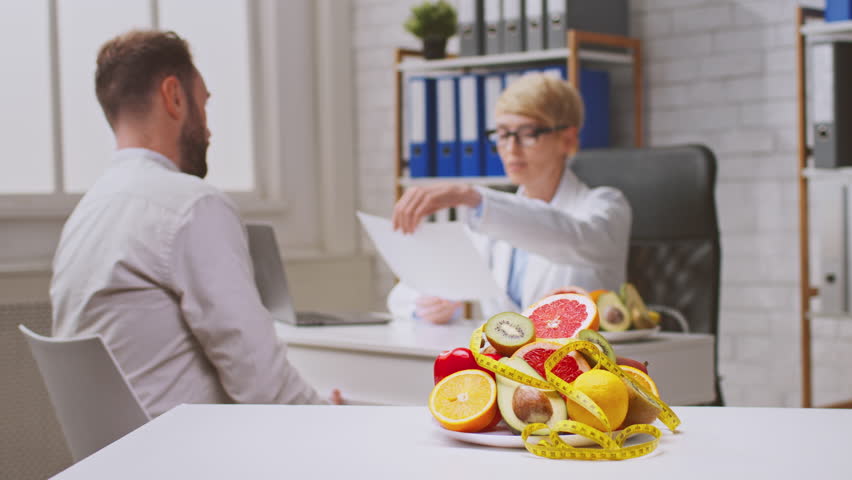 A healthcare professional discusses dietary recommendations with a man patient in a well-lit clinic. Fresh fruits are visible on the table, highlighting the focus on healthy eating and nutrition.