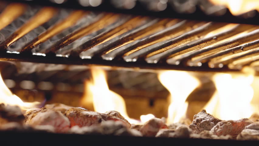 On grill, burning coals create intense heat needed to cook mouth watering dishes. Mesmerizing flames create charming backdrop for festive gathering around sizzling grill. Template for title. AD.