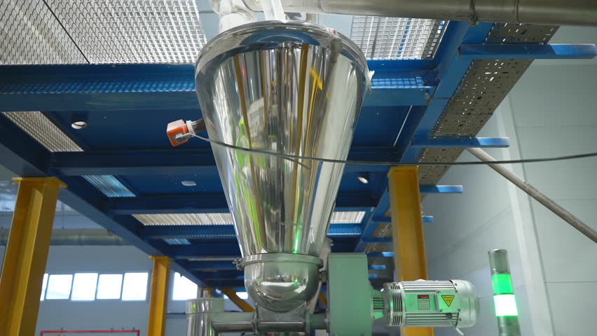 Dry components dispenser made of shiny steel in brightly lit workshop. Pouring materials dosing equipment installed in manufacturing factory