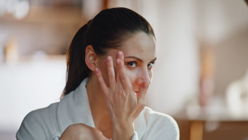 Girl admiring face beauty in home mirror touching beautiful smooth skin closeup. Smiling brunette enjoy cosmetics procedure results looking on glowing appearance. Happy woman looking in reflection.