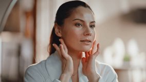 Girl admiring face beauty in home mirror touching beautiful smooth skin closeup. Smiling brunette enjoy cosmetics procedure results looking on glowing appearance. Happy woman looking in reflection. - Powered by Shutterstock - Get 15% off with code: PIKWIZARD15