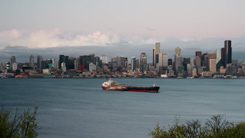 Time-lapse of downtown Seattle at sunset, captured from across Elliott Bay. A large cargo ship passes through the water in front of the iconic skyline.