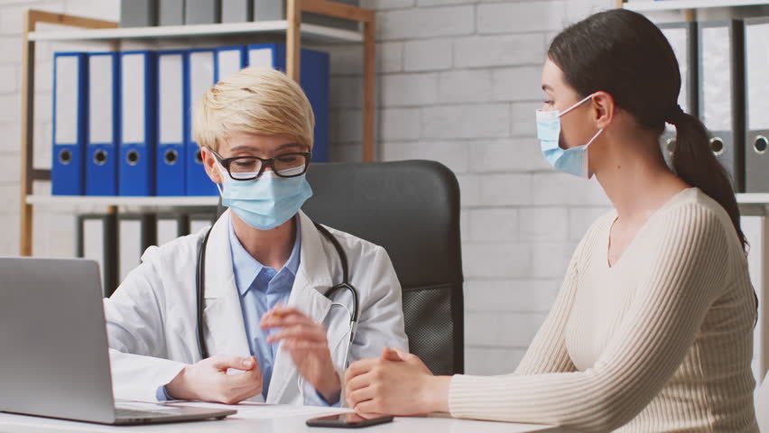 A dietitian is advising a client on nutrition choices in a contemporary clinic setting. Both individuals are wearing masks, ensuring a safe environment during the consultation.