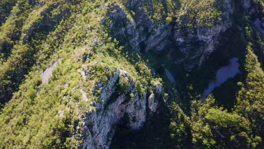 An aerial view of a winding road passing through rocky mountains in Iron Gates Natural Park in southwestern Romania on a sunny day