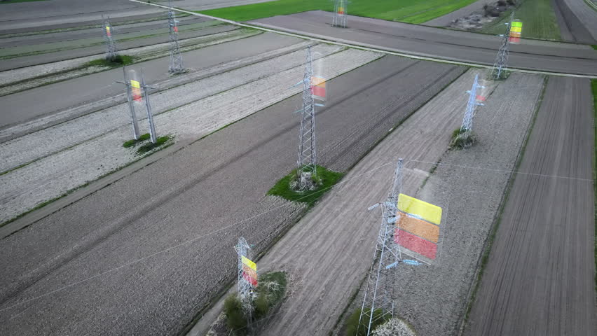 Orbit drone footage of power pylons crossing cultivated fields with energy color overlays indicating usage levels