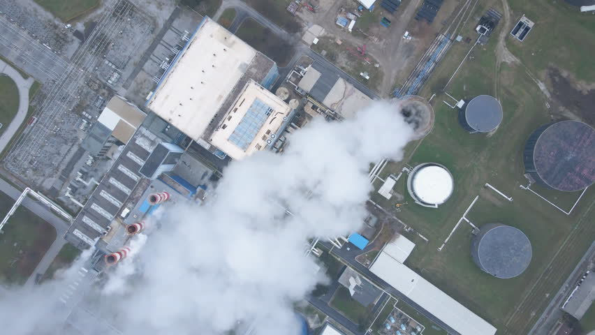 Industrial facility emits dense white smoke while a red graph overlay shows air pollution trend decline over time