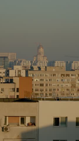 Vertical Screen: Observe the skyline of Bucharest with residential apartment blocks and the prominent National Salvation Cathedral in the background during golden hour.